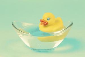 un canard en caoutchouc jaune nage dans un bain sur fond émeraude. photo