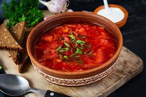 bortsch ukrainien traditionnel avec oignon vert et crème sure. délicieuse soupe de betteraves dans un bol avec du pain de seigle photo