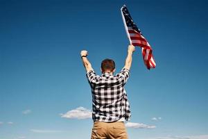 l'homme tient le drapeau national des états-unis contre le ciel bleu photo