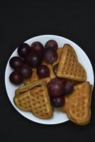 délicieuses gaufres et raisins sur une assiette. un petit-déjeuner sucré composé de gaufres et de raisins rouges. gaufres en forme de cœur. photo