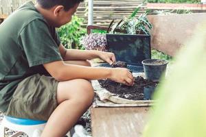 garçon apprend à faire pousser des fleurs dans des pots grâce à l'enseignement en ligne. pelleter le sol dans des pots pour préparer les plantes pour la plantation du concept d'activités de loisirs photo