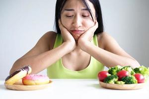 les belles femmes asiatiques choisissent entre les légumes et les beignets. perdre du poids photo