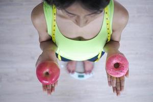 femme mesurant le poids corporel sur une balance tenant un beignet et une pomme. les sucreries sont de la malbouffe malsaine. alimentation saine, mode de vie. perte de poids. photo