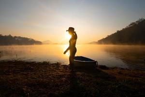 femmes debout à côté d'un bateau vers le rivage au réservoir pendant le lever du soleil, parc forestier de harirak huai nam man reservoir loei thailand 21 jan 2023 photo