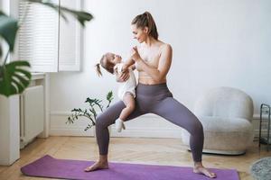 jeune femme fit maman avec bébé fille dans ses bras faisant du fitness sur tapis à la maison photo