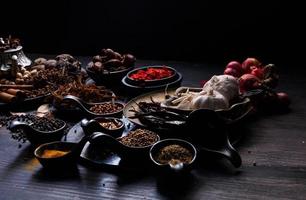 photo vue de dessus beaucoup d'ail, d'oignons, de poivrons, de piment et d'herbes séchées, ont été placés sur des assiettes et des tasses sur un fond de drak en bois noir. a été divisé pour se préparer à cuisiner des aliments indiens des aliments sains