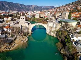 vue aérienne par drone du vieux pont de la ville de mostar en bosnie-herzégovine pendant la journée ensoleillée. couleurs bleu turquoise de la rivière neretva. Patrimoine mondial de l'UNESCO. personnes marchant sur le pont. photo