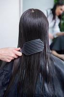 le coiffeur applique un masque capillaire sur les cheveux noirs raides. soins capillaires au salon de beauté. photo