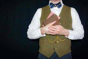 portrait d'homme en gilet de tweed et noeud papillon tenant de vieux livres sur fond noir. amour de la littérature et de la lecture. photo