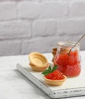 caviar rouge dans un bocal en verre et tartelettes rondes sur un tableau blanc photo