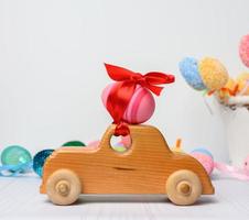 Petite voiture en bois transportant un oeuf de Pâques rose fixé avec un ruban rouge photo