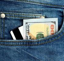 dollars américains en papier et carte bancaire en plastique à bande magnétique dans la poche d'un jean bleu photo
