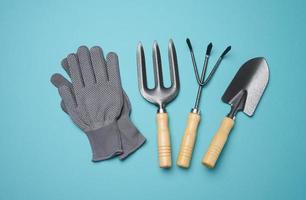 outils de jardin pour le traitement des lits dans le jardin et gants textiles sur fond bleu photo