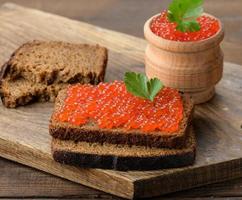 le caviar de saumon rouge repose sur un morceau de pain de seigle. table en bois marron photo