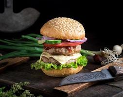 cheeseburger avec des légumes sur une vieille planche de bois marron photo