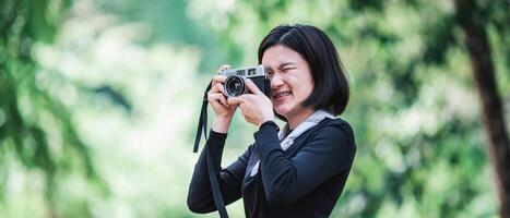 jeune jolie femme utilise un appareil photo pour prendre des photos dans le parc naturel
