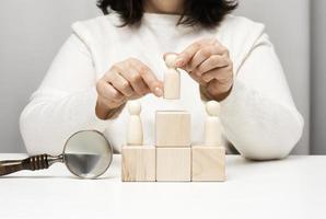 une femme en pull blanc met une figurine en bois sur le podium. le concept de recherche d'employés, d'avancement de carrière. employé talentueux photo