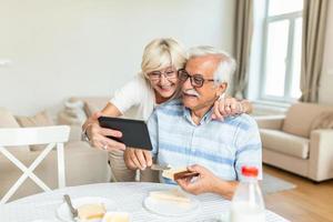 heureux couple d'âge mûr utilisant une tablette numérique et agitant tout en ayant un appel vidéo à la maison.un couple âgé faisant un appel vidéo sur un pavé tactile tout en prenant son petit déjeuner à la maison. photo