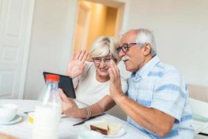 un homme âgé et sa femme utilisent une tablette numérique et communiquent avec leurs enfants. un couple de personnes âgées heureux prend son petit déjeuner et a une conversation en ligne avec sa famille et envoie des salutations. photo