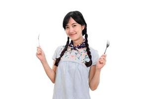 portrait de la belle jeune femme asiatique sourire en robe denim avec cuillère et fourchette sur fond blanc photo