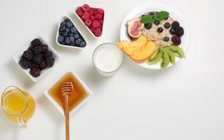 lait, assiette avec bouillie d'avoine et fruits, jus fraîchement pressé dans une carafe en verre transparent, miel dans un bol sur une table blanche. petit-déjeuner sain photo