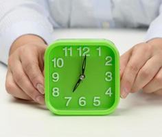 femme main détient une vert carré alarme horloge, le l'horloge spectacles Sept dans le Matin. réveiller en haut tôt, début le journée photo