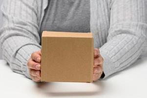 deux femelle mains tenir une carré boîte fabriqué de marron ondulé papier carton sur une blanc arrière-plan, proche en haut photo