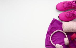 une paire de textile violet des sports baskets, sans fil écouteurs, une serviette et une bouteille de l'eau sur une blanc Contexte. tenue de sport photo