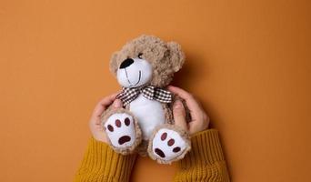 femelle main tenir une petit marron jouet nounours ours sur une marron Contexte photo