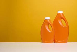 Deux bouteilles en plastique orange avec détergent liquide se tiennent sur un tableau blanc, fond jaune photo