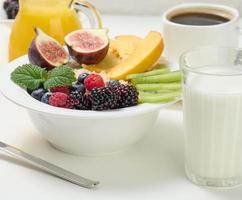 assiette complète avec flocons d'avoine et fruits, jus fraîchement pressé dans une carafe en verre transparent, tasse de café sur un tableau blanc. petit-déjeuner sain photo