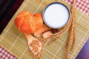 Lait dans bol avec croissant cuit pain, soja haricot sur cuillère et épices sur en bois bambou. copie espace pour texte. Haut vue photo