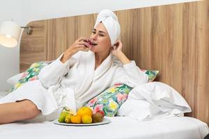 femme dans peignoir de bain ayant des fruits sur lit photo