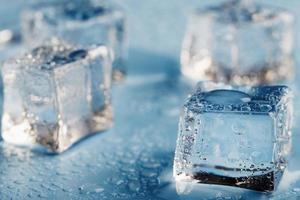 cubes de glace en gros plan avec des gouttes d'eau de fonte dispersées sur un fond bleu. photo