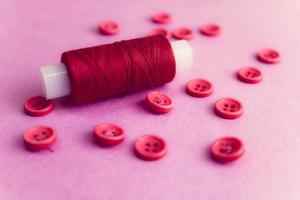 belle texture avec de nombreux boutons roses ronds pour la couture, la couture et une bobine de fil. espace de copie. mise à plat. fond rose, violet photo