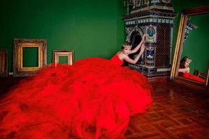 belle femme en robe longue rouge et en couronne royale près de la cheminée dans un intérieur de luxe en studio photo