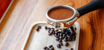 équipement d'outil de café barista inviolable et café tempéré dans des grains de café torréfiés de porte-filtre sur une table en bois photo