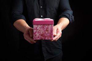 adulte homme dans une noir chemise détient une rose carré boîte avec une arc photo