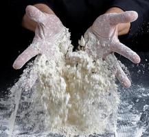 le chef en uniforme noir verse de la farine de blé blanc de ses mains photo