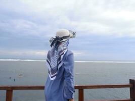 dos de la femme au chapeau sur la plage tropicale qui regardait le ciel et la mer depuis le pont. vue sur la mer photo