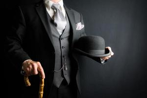 homme dans foncé gris costume en portant melon chapeau et parapluie sur noir Contexte. ancien style et rétro mode de élégant Anglais gentilhomme. photo