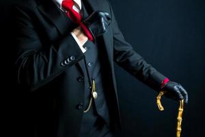 portrait de élégant gentilhomme dans noir costume et cuir gants penché sur parapluie sur noir Contexte. ancien style et rétro mode. photo