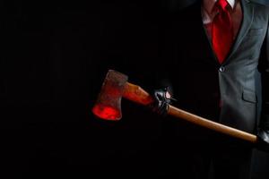 portrait de homme d'affaire dans foncé costume et cuir gants en portant sanglant rouge hache. concept de horreur film tueur. photo