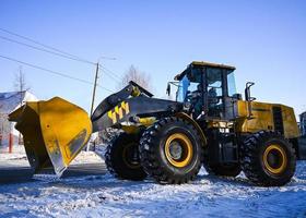 Tractopelle chargeur sur le route. une Jaune tracteur supprime neige sur le rue. photo