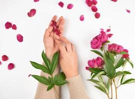 deux mains de une Jeune fille avec lisse peau et une bouquet de rouge pivoines photo