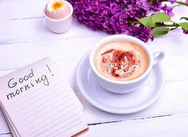 cappuccino dans une blanc tasse, suivant Remarque avec le une inscription bien Matin photo