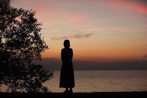 silhouette d'une femme debout seule au bord de la mer pendant le coucher du soleil photo