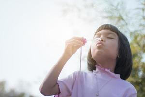 mignon enfant asiatique soufflant des bulles dans le parc photo