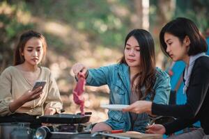 les jeunes femmes cuisinent et utilisent un smartphone pour prendre des photos en camping