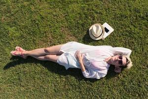 Haut vue de au dessus de une femme mensonge et relaxant sur une Prairie couvert avec vert herbe sur une ensoleillé été ou printemps journée. photo